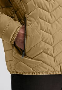 Braune gesteppte Jacke mit einer mit Reißverschluss gesicherten Tasche, elastischen Bündchen und einer strukturierten Oberfläche. Das Design enthält ein Chevron-Muster für den gesamten Jacke.