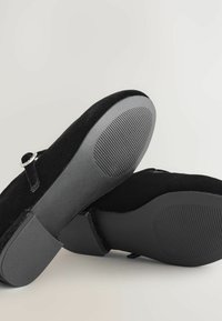 Pantofi din suede negru cu talpă plată din cauciuc, dotati cu o curea cu un accent de cataramă și detalii texturate pe talpă pentru aderență.