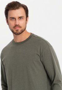 Olivgrön långärmad t-shirt gjord av mjukt, lättviktigt tyg med rund hals och avslappnad passform, med subtila sömnadsdetaljer.