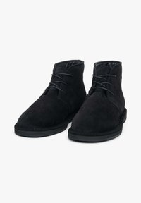 Czarne zamszowe botki za kostkę z zaokrąglonym noskiem, sznurowaniem z przodu i teksturowanym wykończeniem. Posiadają płaską czarną gumową podeszwę oraz przeszycia jako zdobienie.