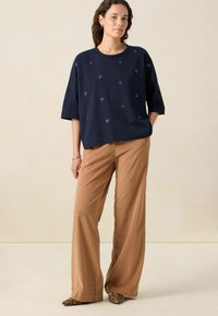 Marineblauwe katoenen t-shirt met korte, brede mouwen, versiert met verspreide bloemembroidery. Gecombineerd met lichtbruine corduroy wijde broeken.