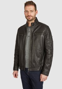 Schwarze Lederjacke mit Stehkragen, Reißverschluss auf der Vorderseite, zwei Brusttaschen und gerippten Akzenten an den Ärmeln. Getragen über einem grauen Henley-Shirt.