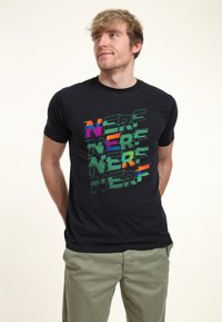 Sort kortærmet t-shirt med ordet "NERF" i flerfarvet, overlappende tekst med forskellige skrifttyper og størrelser. Casual pasform, glat tekstur.