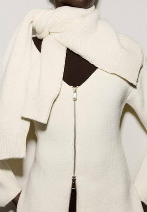Suéter de punto blanco con cierre de cremallera y escote en V, que incluye una bufanda de punto a juego situada alrededor del cuello. Textura suave y detalles acanalados.