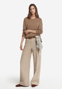 Brun långärmad topp i kombination med beige vida byxor. Brun bälte med en mönstrad scarf i midjan. Mjuka texturer, neutrala färger.