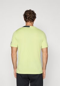 Camiseta deportiva de manga corta verde claro con un detalle en el cuello gris oscuro en contraste, fabricada con un material suave y transpirable.