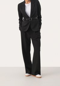 Veste noire cintrée avec une ceinture à la taille, associée à un pantalon noir ample et des baskets blanches. Design minimaliste aux lignes épurées.