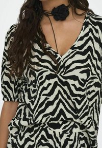 Blůza se zebra vzorem v černobílém provedení s hlubokým V výstřihem a krátkými nabíranými rukávy, s texturovaným plisovaným designem.