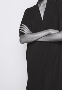 Svart knälång klänning med korta ärmar och v-ringning, som har en avslappnad passform och mjuk textur, idealisk för komfort och avslappnad användning.