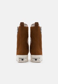 Rudi zomšos aukšti sportbačiai su užtrauktuku, baltais gumos padais ir Chuck Taylor logotipu ant kulno. Tekstūruota danga su minkštu išvaizda.