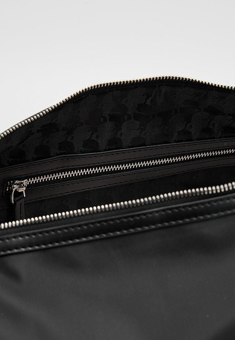 Interior de bolsa de nylon negra con textura lisa, dos bolsillos con cremallera y un forro estampado con detalles sutiles. Herrajes de cremallera plateados.