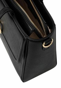 Borsa a mano in pelle nera con forma strutturata. Caratterizzata da hardware color oro, doppi scomparti con zip e un dettaglio ad anello laterale.