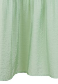 Tissu vert clair texturé avec une finition lisse, tombant doucement ; doté d'un ourlet arrondi et d'une taille froncée pour une fluidité.