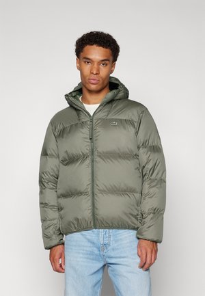 Veste matelassée verte avec des coutures horizontales, une capuche et une fermeture éclair devant. Présente un petit logo en accent sur la poitrine gauche.