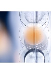 Klara glasbägare staplade vertikalt, innehållande vätskor: en ljus orange vätska med bubblor, en klar vätska nedanför och ett texturerat vitt ämne ovanpå.