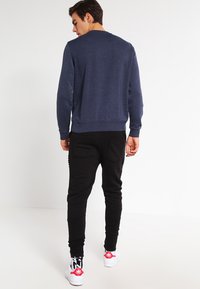 Sudadera azul marino con cuello redondo, puños y dobladillo de canalé, combinada con pantalones joggers negros con bolsillos traseros y zapatillas blancas con detalles rojos.