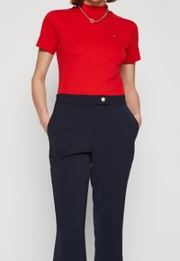 Czerwony bawełniany t-shirt z krótkim rękawem, wysokim dekoltem i małym logo. Granatowe spodnie o gładkiej fakturze z złotą spinką w pasie.