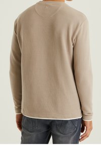 Dlouhý rukáv, světle béžová mikina s texturovaným povrchem. Má rounded výstřih a viditelné švy na zadní straně.