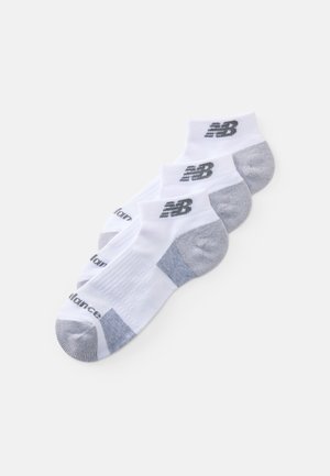 Chaussettes de sport blanches avec des accents gris, portant un logo et une texture côtelée. Conçues pour le confort et la performance, vendues par paquet de trois.