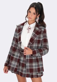 Karierte Blazer- und Rockkombination in Burgunder, Schwarz und Weiß. Der Blazer hat große Revers und zwei Knöpfe; der Rock zeichnet sich durch ein plissiertes Design aus.