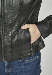 Schwarze Lederjacke mit einem Reißverschluss vorne und Seitentaschen, mit einer strukturierten Oberfläche und taillierter Passform, kombiniert mit blauen Jeans.