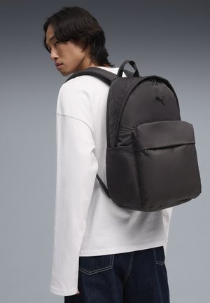 Zaino in tessuto nero con spallacci imbottiti e tasca frontale. Presenta un design arrotondato e il logo PUMA sulla parte superiore.