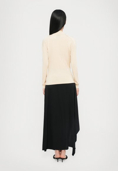 Langschedige, beige top gecombineerd met een zwarte, vloeiende maxi rok. De stof lijkt zacht met een subtiele val en heeft een high-low ontwerp.