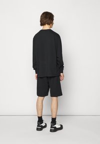 Haut à manches longues noir et short en tissu doux. La tenue présente une coupe décontractée, avec un col ras du cou et un design minimaliste.