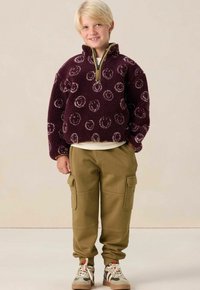 Paarse fleece pullover met smiley face patroon, kwart rits, gecombineerd met lichtbruine cargobroek met zijzakken en beige sneakers.