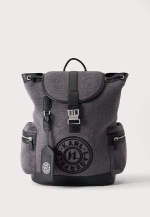 Sac à dos en feutre gris et noir avec rabat avant, deux poches latérales zippées, une poignée supérieure, une boucle à l'avant et un logo circulaire Karl Lagerfeld.