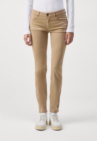Chino en coton beige mélangé avec une coupe slim, design à cinq poches, fermeture à bouton avant et texture lisse, associés à des baskets blanches.