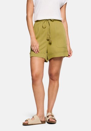 Mujer con shorts de tiro ajustable color verde oliva con bolsillo frontal y dobladillo enrollado, sandalias beige abiertas en la punta y camiseta blanca de manga corta.