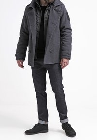 Szary płaszcz dyplomatka z mieszanki wełny z dwoma rzędami guzików, naszywką na rękawie, zestawiony z ciemnymi dżinsami i czarnymi botkami do kostki z podwiniętymi mankietami.