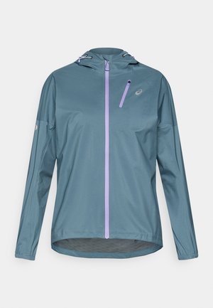 Lahka tekaška jakna morsko zelene barve z vijoličnim zadrgo, nastavljivo kapuco in elastičnimi manšetami. Ima majhen žep z zadrgo na prsih.