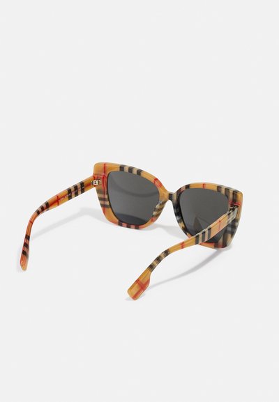 Óculos de sol estilo gato com uma armação laranja e preta com padrão, lentes cinzas e hastes texturizadas. Listas horizontais distintas nas laterais.