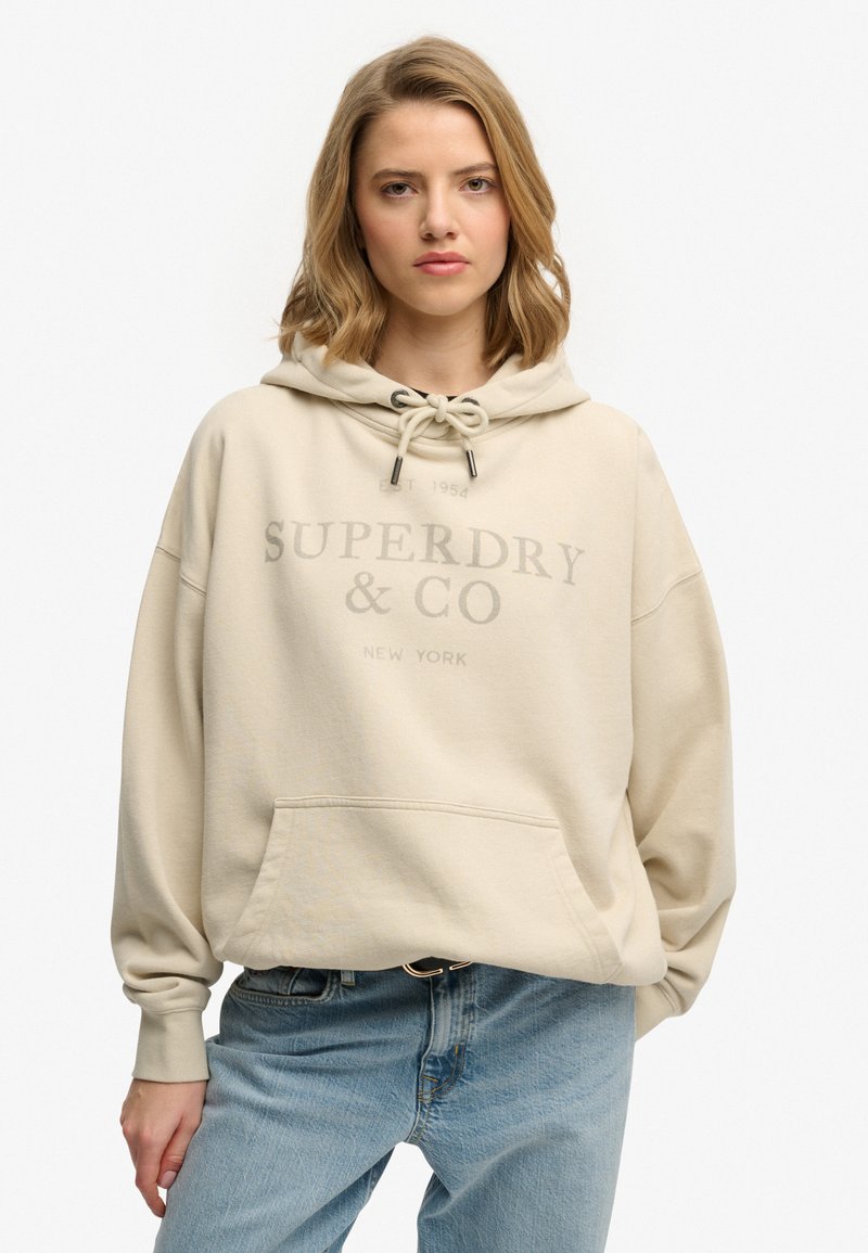 Beżowa bluza z kapturem wykonana z mieszanki bawełny, z przednią kieszenią typu kangurka, kapturem ze sznurkiem oraz logo "SUPERDRY & CO" w stonowanym nadruku.