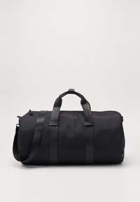 Bolsa de deporte negra hecha de nylon texturizado, con dos asas superiores, una correa de hombro desmontable y un diseño minimalista sin hardware visible.