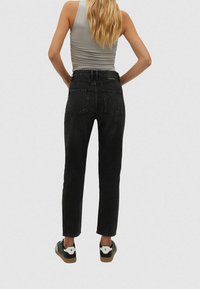 Zwarte denim jeans met een hoge taille, rechte pijpen en een klassiek vijf-pocket ontwerp. Draagt een grijze tanktop en zwarte sneakers.