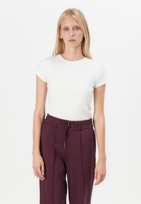 T-shirt blanc ajusté à rayures avec des manches courtes, associé à un pantalon taille haute bordeaux avec cordon de serrage et détails plissés.