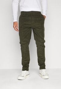 Olivgröna kordflöjtsbyxor med slim fit, som har framfickor, knappstängning och uppvikta anklel. De är kombinerade med vita sneakers.