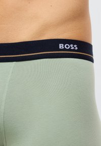 Zielone majtki z mieszanki bawełny z granatowym paskiem w talii z białym logo "BOSS" i złotą linią ozdobną. Gładka faktura, dopasowany krój.