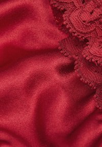Tissu satin rouge profond avec une bordure en dentelle complexe le long du bord, créant un contraste texturé. Surface lisse avec un éclat subtil.