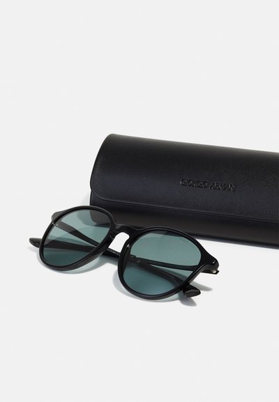 Mustat aurinkolasit pyöreillä sangoilla ja vihreillä linsseillä, yhdessä mustan nahkaisen kotelon kanssa, johon on painettu "Giorgio Armani".