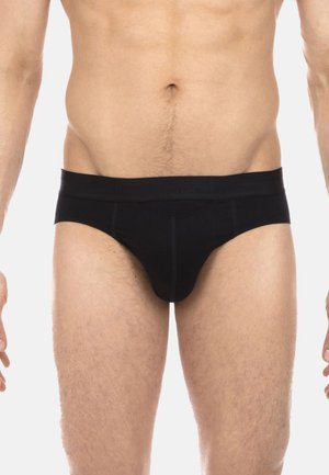 Mannelijke torso en bovenbenen in zwarte slips met zichtbare stiksels en een elastische tailleband tegen een witte achtergrond.