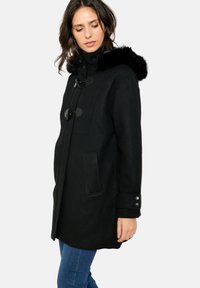 Črn volnen plašč z oblazinjeno kapuco, toggl gumbe, stranske žepke in detajle na manšetah. Srednje dolga zasnova, primerna za hladnejše vreme.