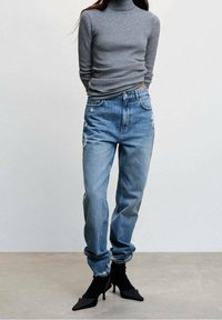 Pull col roulé gris clair associé à un jean bleu déchiré, avec une coupe ample, des revers retroussés et des bottines à talons aiguilles noires.