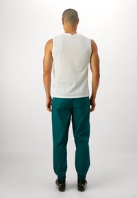 Top bianco senza maniche e pantaloni tapered teal, con polsini elasticizzati e texture liscia. Design semplice, senza motivi o hardware visibili.