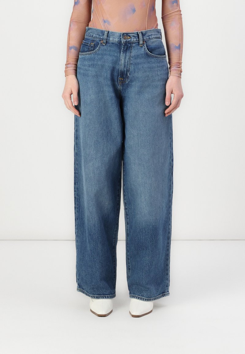 Lys blå denim brede bukser med høy midje, med fem lommer og knappelukking, kombinert med hvite spisse sko.