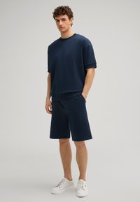 Marineblauwe katoenen T-shirt met ronde hals en korte mouwen, gecombineerd met bijpassende knielange shorts en witte sneakers. Eenvoudige, ontspannen pasvorm.