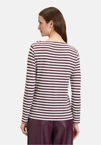 Langsleeve top met horizontale bordeauxrood en witte strepen, een brede halslijn en een ontspannen pasvorm, gecombineerd met hoog geïdechte paarse broek.